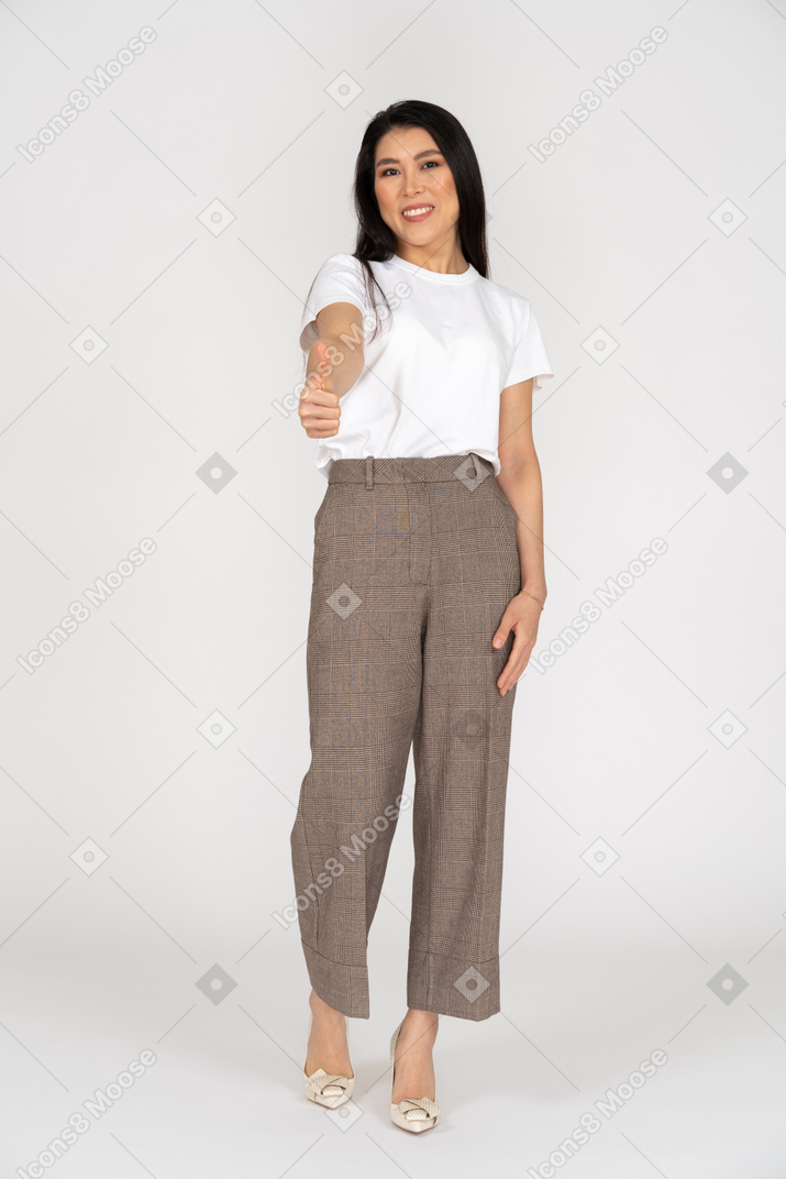 Vista frontale di una giovane donna sorridente in calzoni e t-shirt che mostra il pollice in su