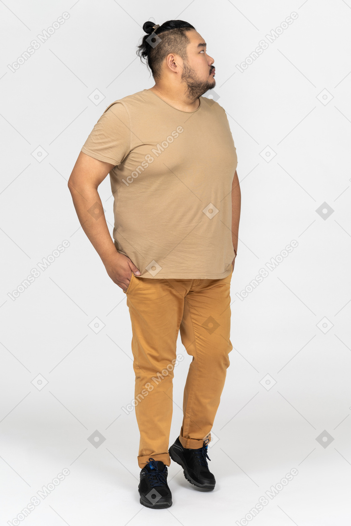 Homem asiático gordo em pé profundamente nos pensamentos e de mãos dadas nos bolsos