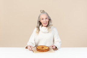 Elegante alte frau mit einem frisch gebackenen kuchen zufrieden