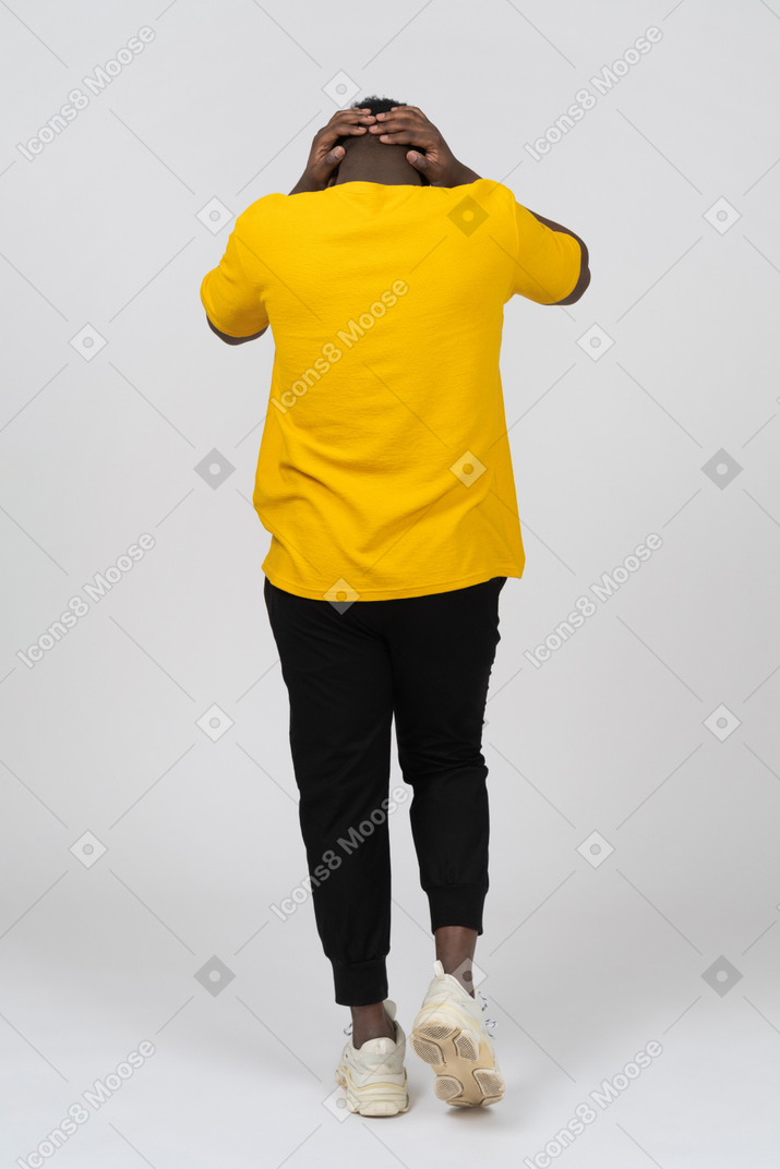 Vista posterior de un joven hombre de piel oscura caminando con camiseta amarilla tocando la cabeza