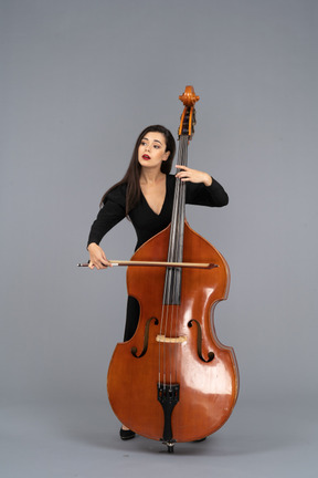Front view of a young woman in black dress playing the double-bass with a bow