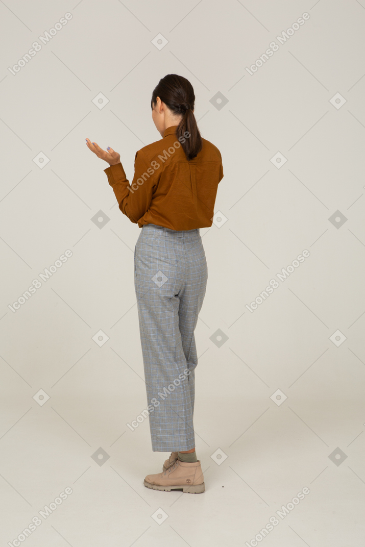 Vista posteriore di tre quarti di una giovane donna asiatica chiedendosi in calzoni e camicetta che alza le mani
