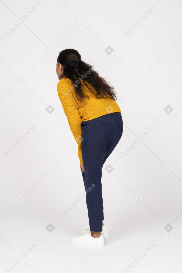 Vista lateral de una niña en ropa casual inclinándose y tocando sus rodillas
