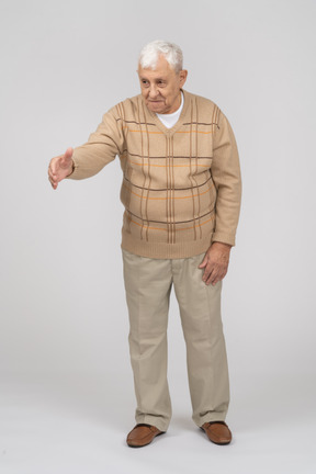 Vista frontale di un vecchio felice in abiti casual che dà una mano per scuotere