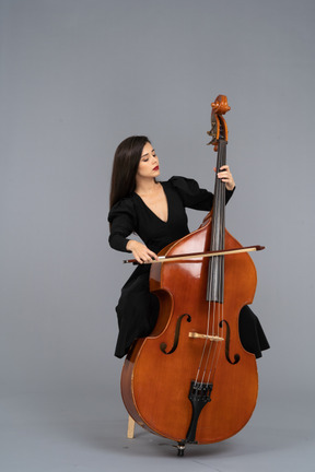 一位年轻的女士，坐在一把椅子上，同时玩一把弓的低音提琴的前视图