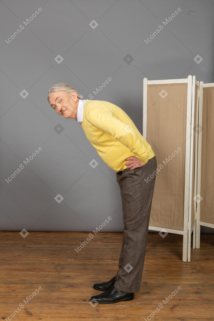 Side view of an old man putting hands on hips while leaning forward