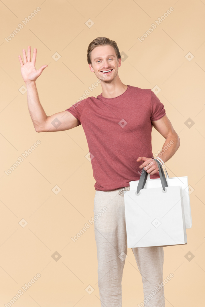 Young guy holding white shopping bags and waving