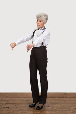 Vista de tres cuartos de una anciana en ropa de oficina poniendo los pulgares hacia abajo