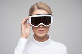 Young blonde woman in white turtleneck adjusting ski goggles