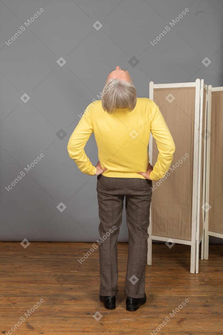 Back view of an old man putting hands on hips while leaning back