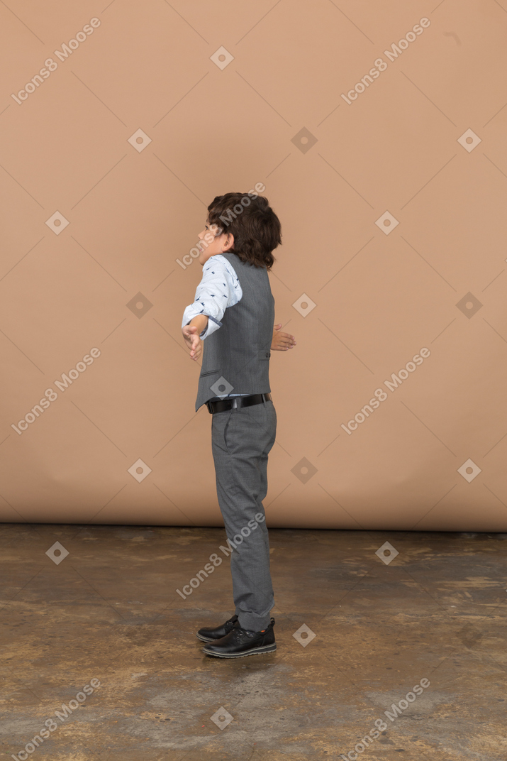 Vista lateral de un niño con traje de pie con los brazos extendidos