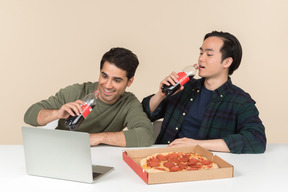Amigos interraciales comiendo comida chatarra y viendo películas en la computadora portátil