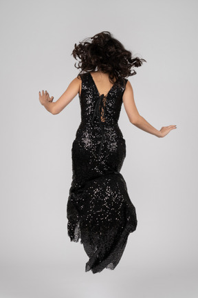 Красивая женщина в черном вечернем платье прыгает