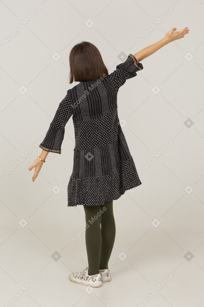 Vista posterior de tres cuartos de una niña en vestido extendiendo sus brazos