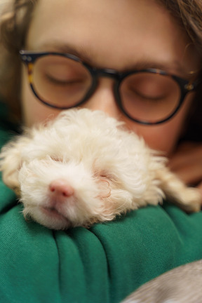 Jovem de óculos, aninhada em seu pequeno poodle e olhando para a câmera