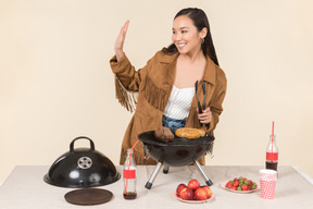 Joven mujer asiática preparando barbacoa y saludando con la mano