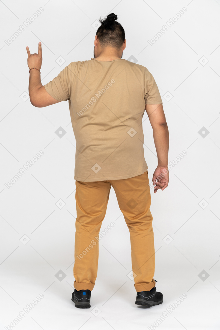 Plump young man making rock gesture back to camera