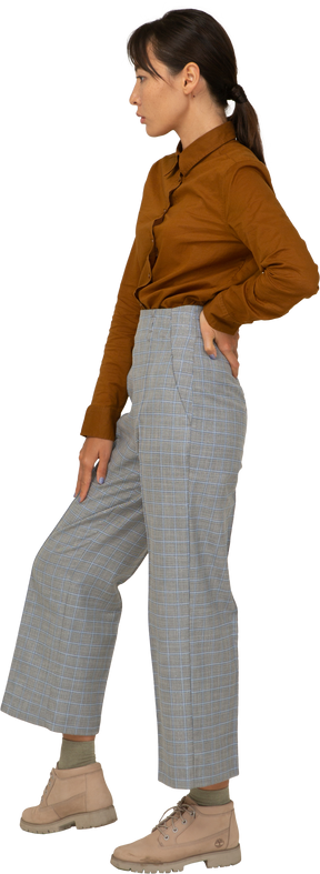 Vista laterale di una giovane donna asiatica in calzoni e camicetta che mette la mano sull'anca