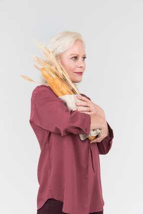 A nice-looking middle-aged blonde woman in a burgundy shirt and with a freshly bought bread in her hands
