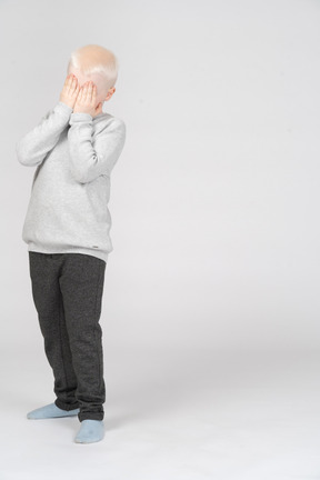 Front view of a scared boy covering face with hands