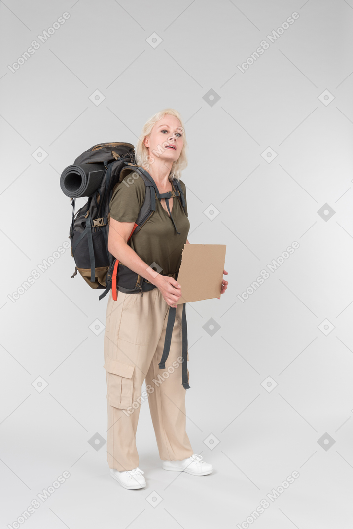 Mature female hitchhiker carrying backpack and holding carton