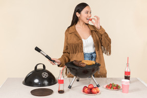 Junge asiatische frau, die bbq tut und erdbeere isst