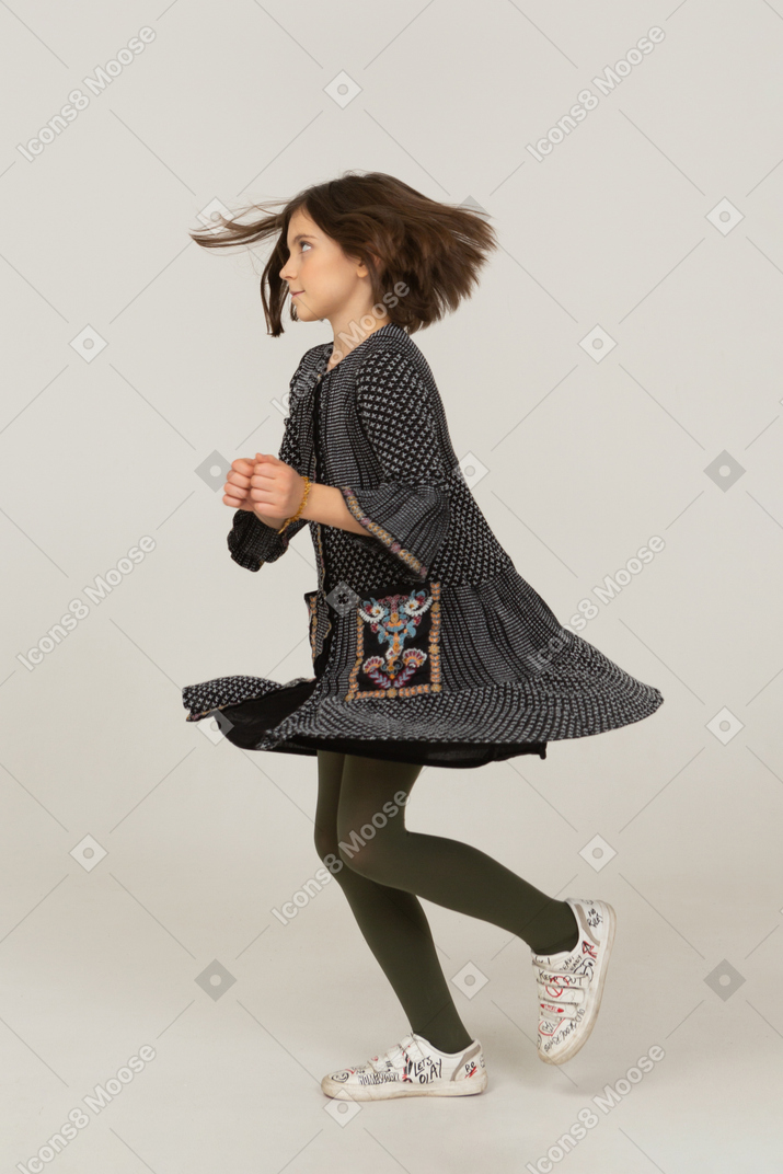 Vista laterale di una bambina che balla con i capelli disordinati che indossa un vestito
