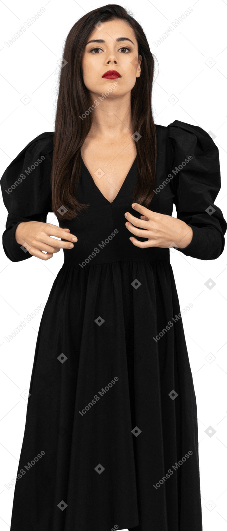 Vista frontale di una giovane donna seria che adegua il suo vestito nero