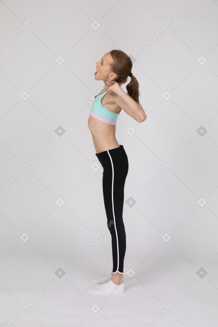 Side view of a tired teen girl in sportswear yawning