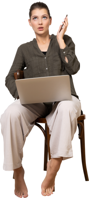 Vista frontale di una giovane donna scioccata seduta su una sedia con un laptop e un cellulare