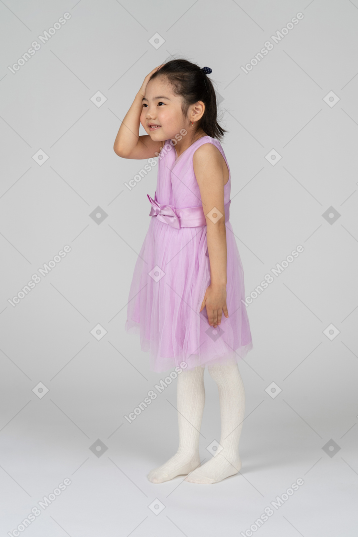 Снимок в три четверти маленькой девочки в милом платье, недоверчиво хлопающей себя по голове