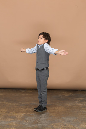 Vista lateral de um menino de terno em pé com os braços estendidos