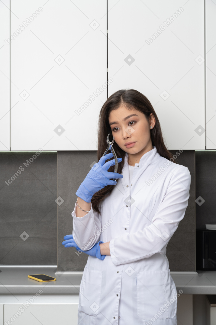 Front view of a tired female doctor holding her dental instrument and looking aside