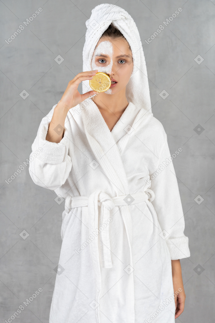 Woman in bathrobe holding a lemon over her mouth