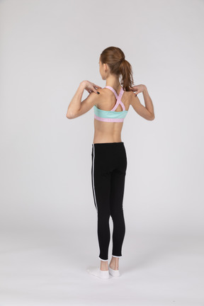 Vista posterior de tres cuartos de una jovencita en ropa deportiva tocando sus hombros