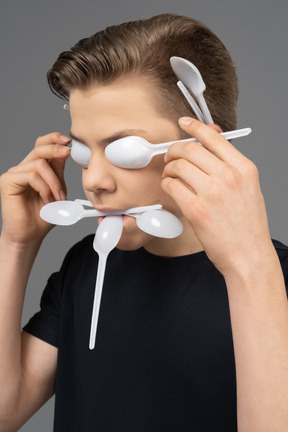Portrait of a male making mask out of plastic spoons