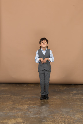Vista frontal de un chico lindo en traje gris mirando a la cámara