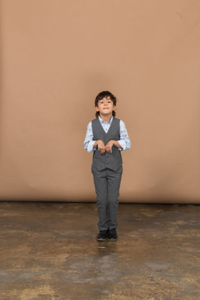 Vue de face d'un garçon mignon en costume gris regardant la caméra