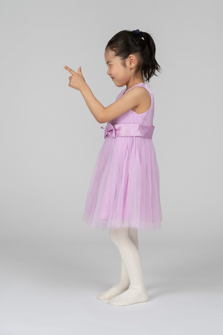 Little girl in pink dress pointing with index finger