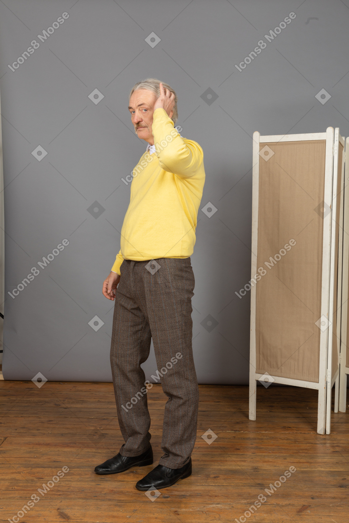 Three-quarter view of an old man in a yellow pullover touching his head