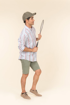 Young caucasian guy standing in profile and holding tennis racket