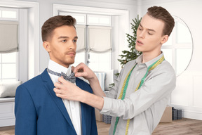 A man helping another man put on his bow tie