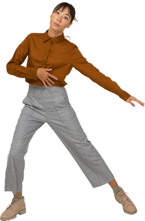 Vista frontal de uma jovem mulher asiática dançando em calça e blusa dando uma estocada