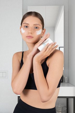 A woman with moisturizer on her face holding a tube