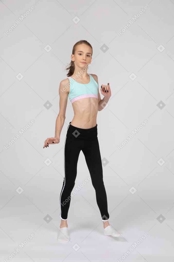 Vista de tres cuartos de una jovencita en ropa deportiva levantando la mano