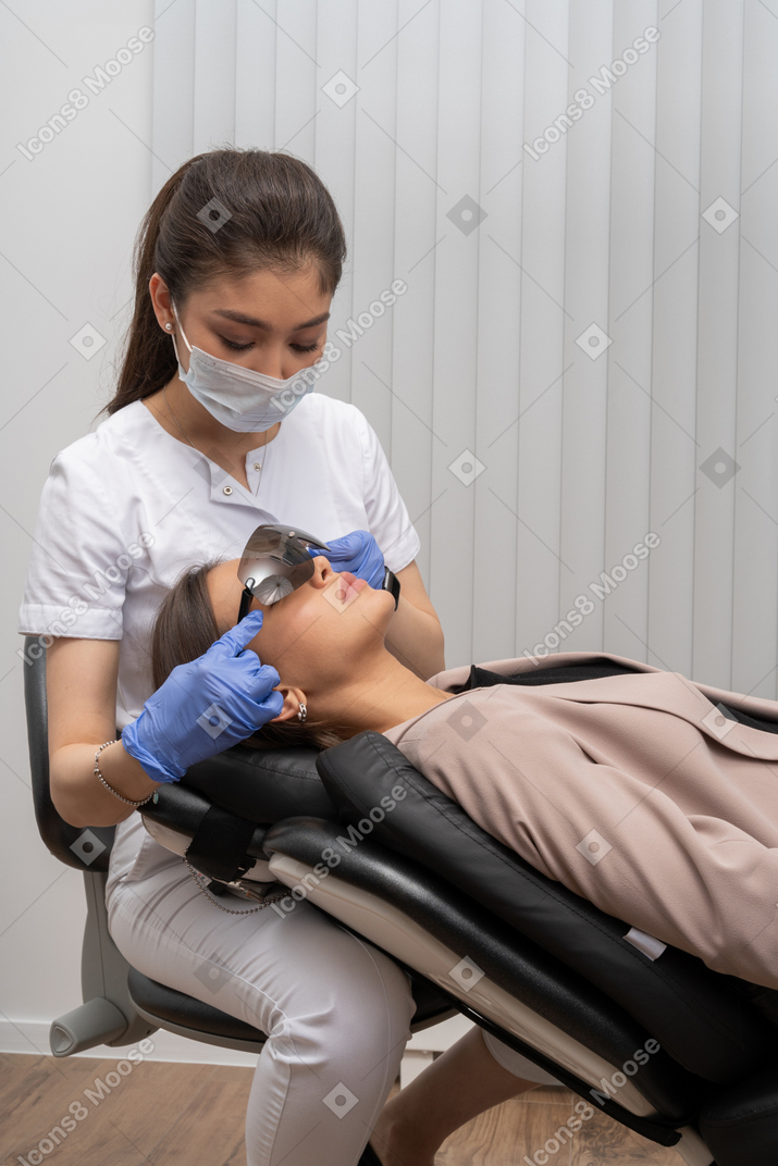 Female dentist in mask and latex gloves putting glasses on her patient