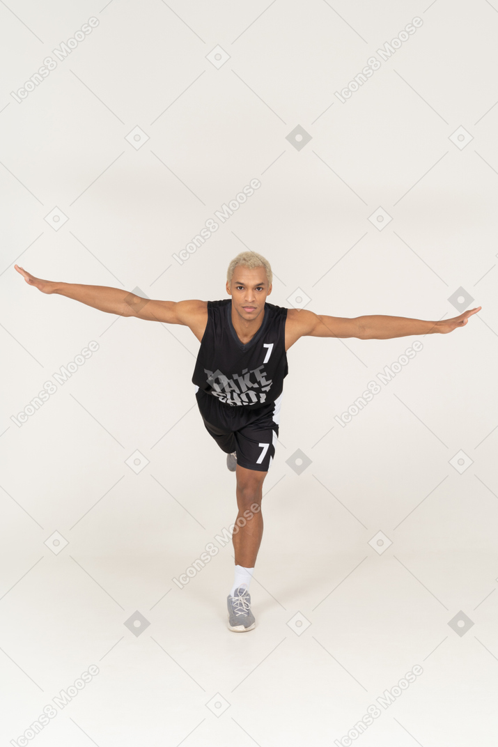 Vista frontal de um jovem jogador de basquete masculino equilibrado, inclinado para a frente e apoiado em uma perna só