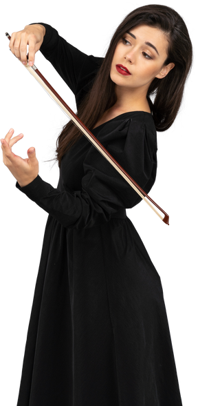 Vista di tre quarti di una giovane donna in abito nero che fa l'impressione di suonare il violino
