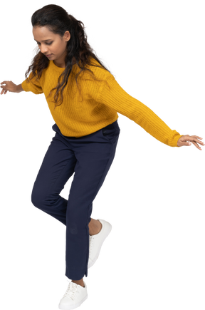 Vista frontal de una niña en ropa casual posando sobre una pierna con los brazos extendidos
