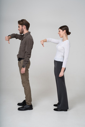 Vista lateral de um jovem casal com roupas de escritório mostrando o polegar para baixo